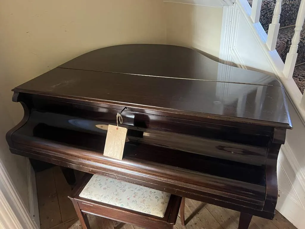 A mahogany baby grand piano photographed where it stands on collection day, beside a staircase