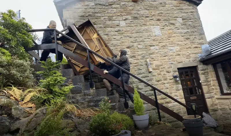 Carrying an upright piano out of a terraced house for disposal